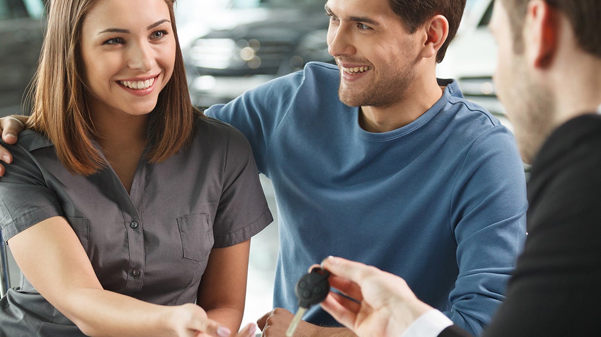 Smiling couple getting new car keys at showroom